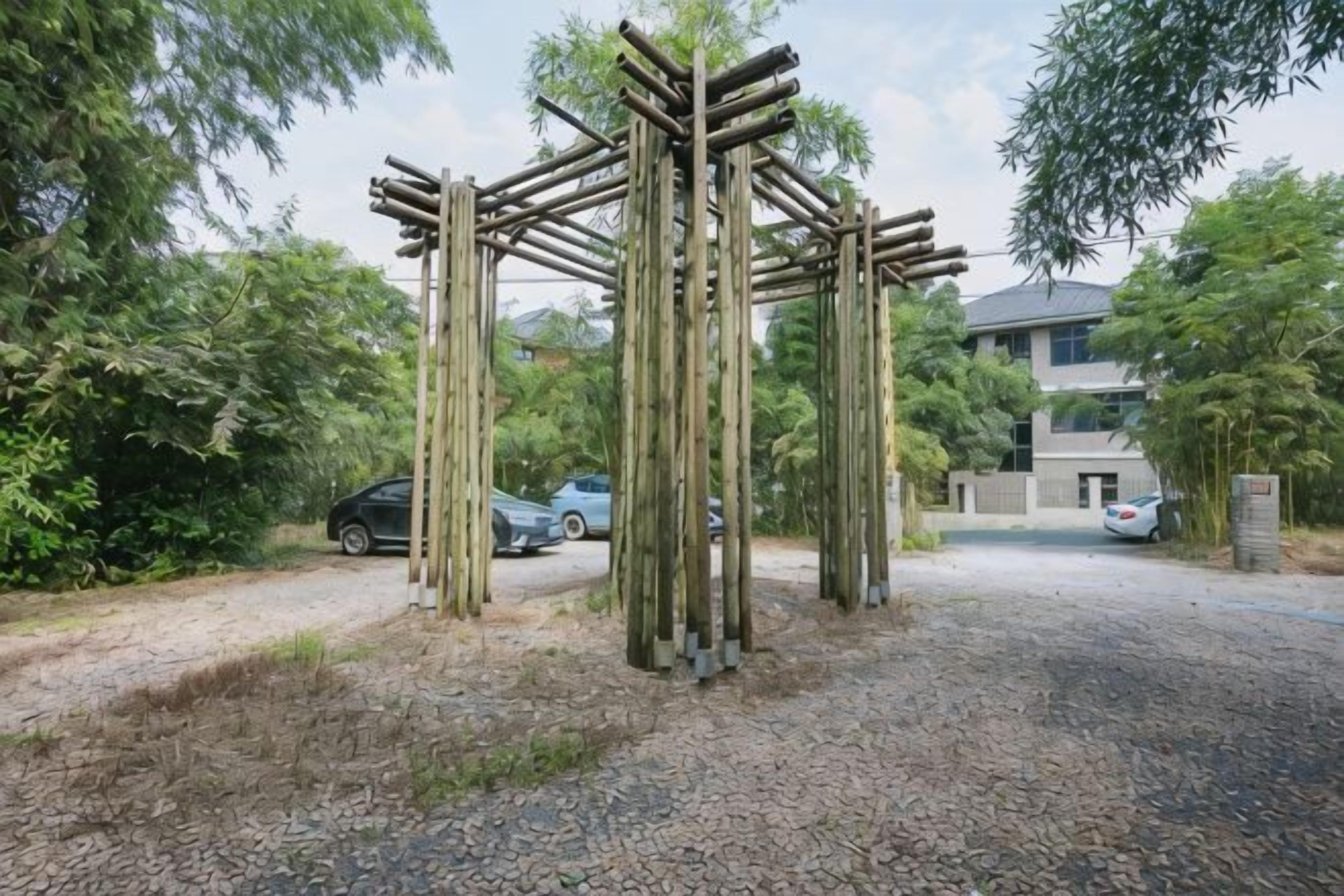 A wooden structure in a garden area with a gravel path and parked cars in the background.