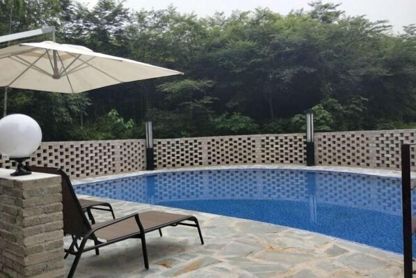 A swimming pool with a tiled edge, a stone deck, a brick wall, and a metal chair. - Zhujiuju Hostel (Deqing)