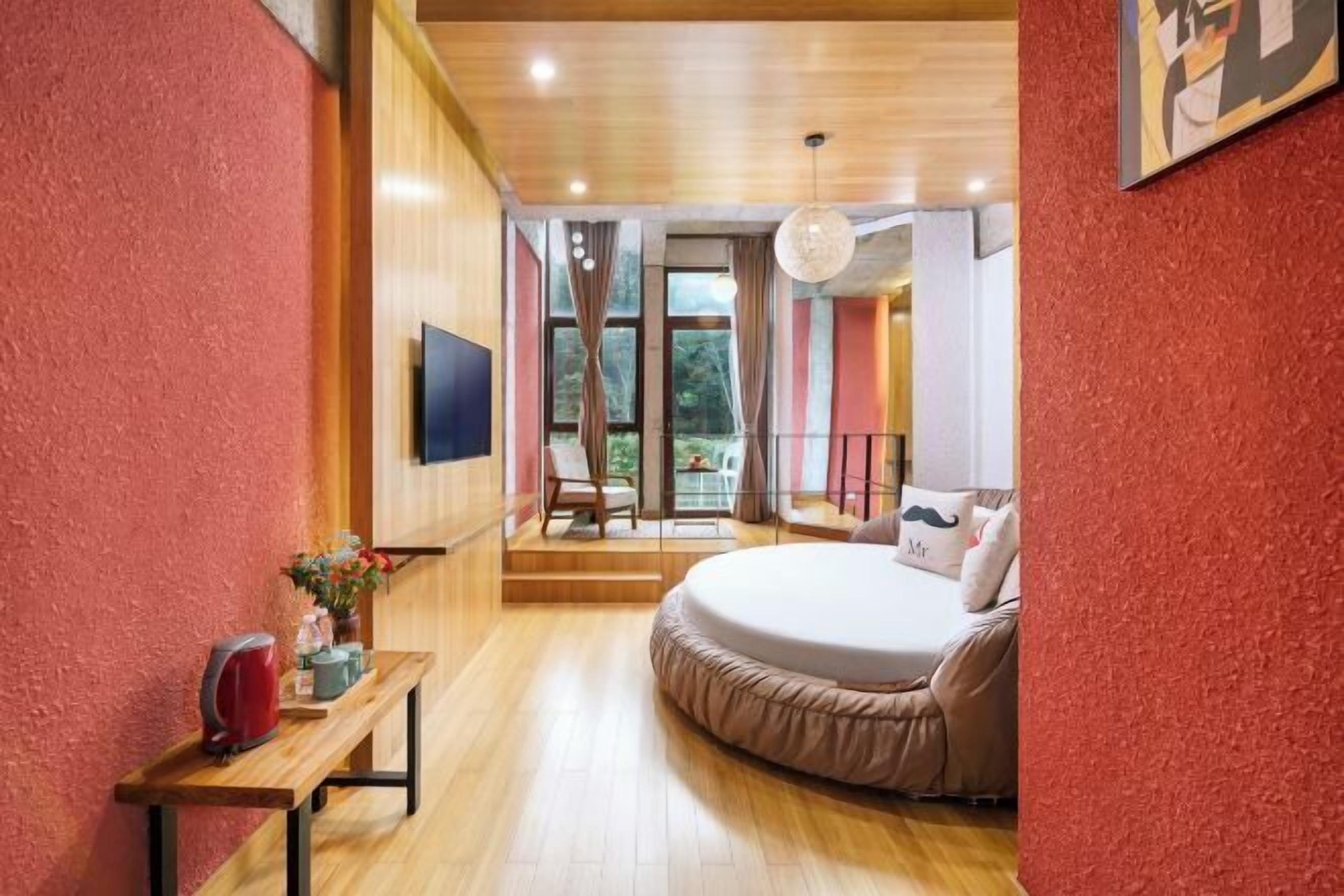 A bedroom with a large bed, a wooden bench, a TV, and a view of the outdoors.