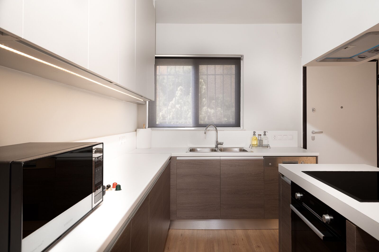 A modern kitchen with a built-in oven, a sink, and a window above it.