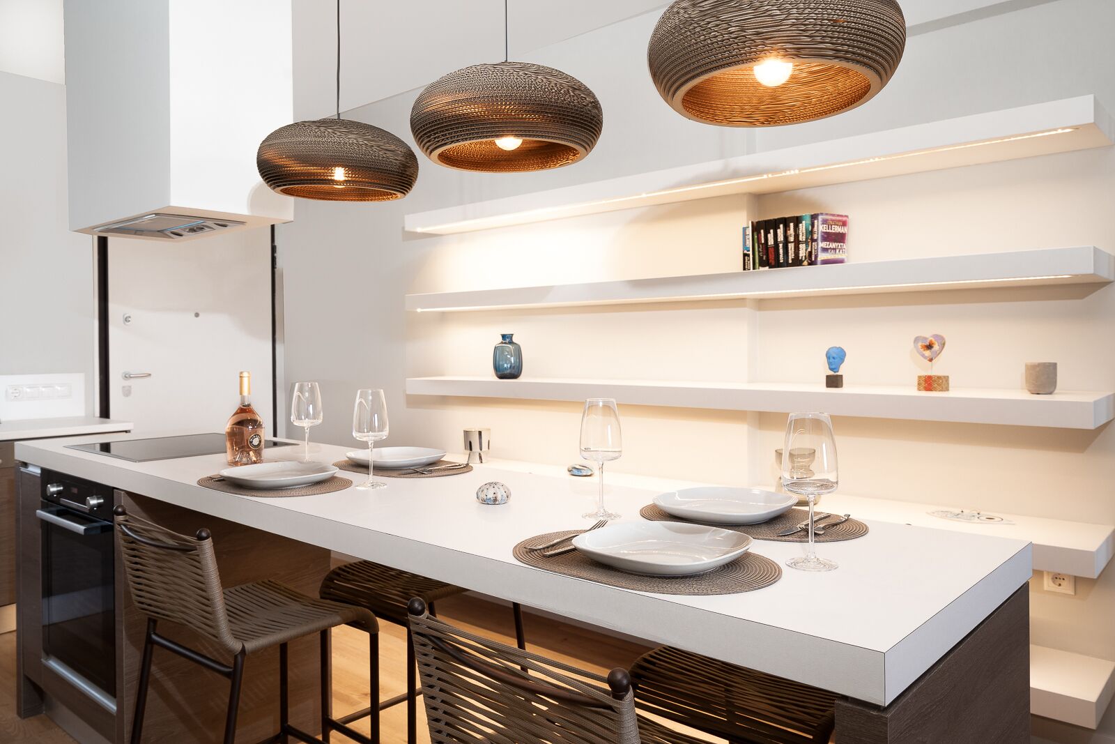 Une cuisine moderne dotée d’un îlot central, de luminaires suspendus et d’étagères intégrées.