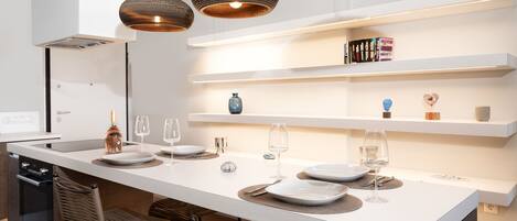 Une cuisine moderne dotée d’un îlot central, de luminaires suspendus et d’étagères intégrées.