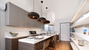 A modern kitchen with a central island, pendant lights, and a built-in oven. - Blue Avra by A&D Properties (Markopoulo Mesogaias)