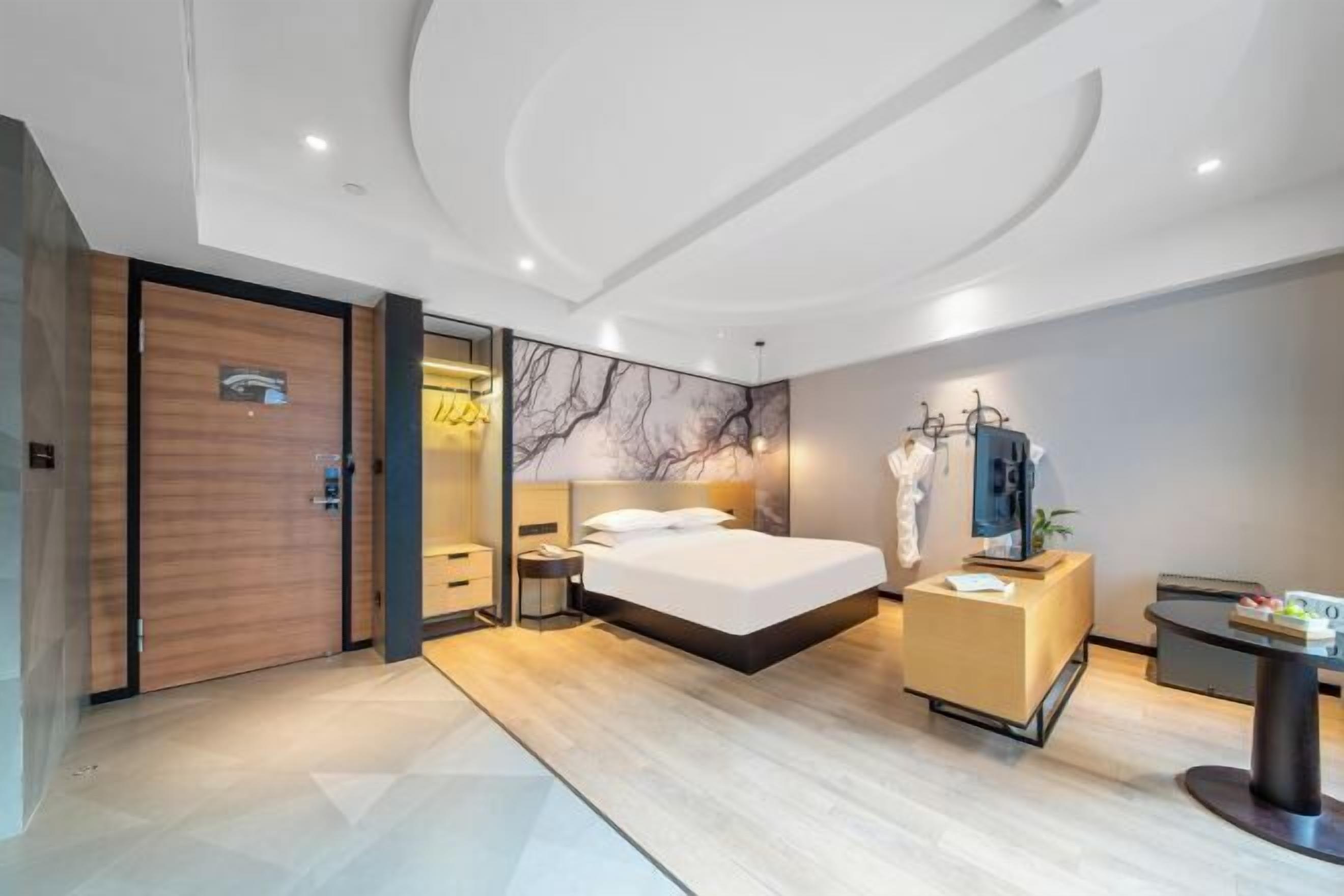 Habitació d'hotel moderna amb un llit gran, un armari de fusta, una taula de nit, un escriptori i una televisió.