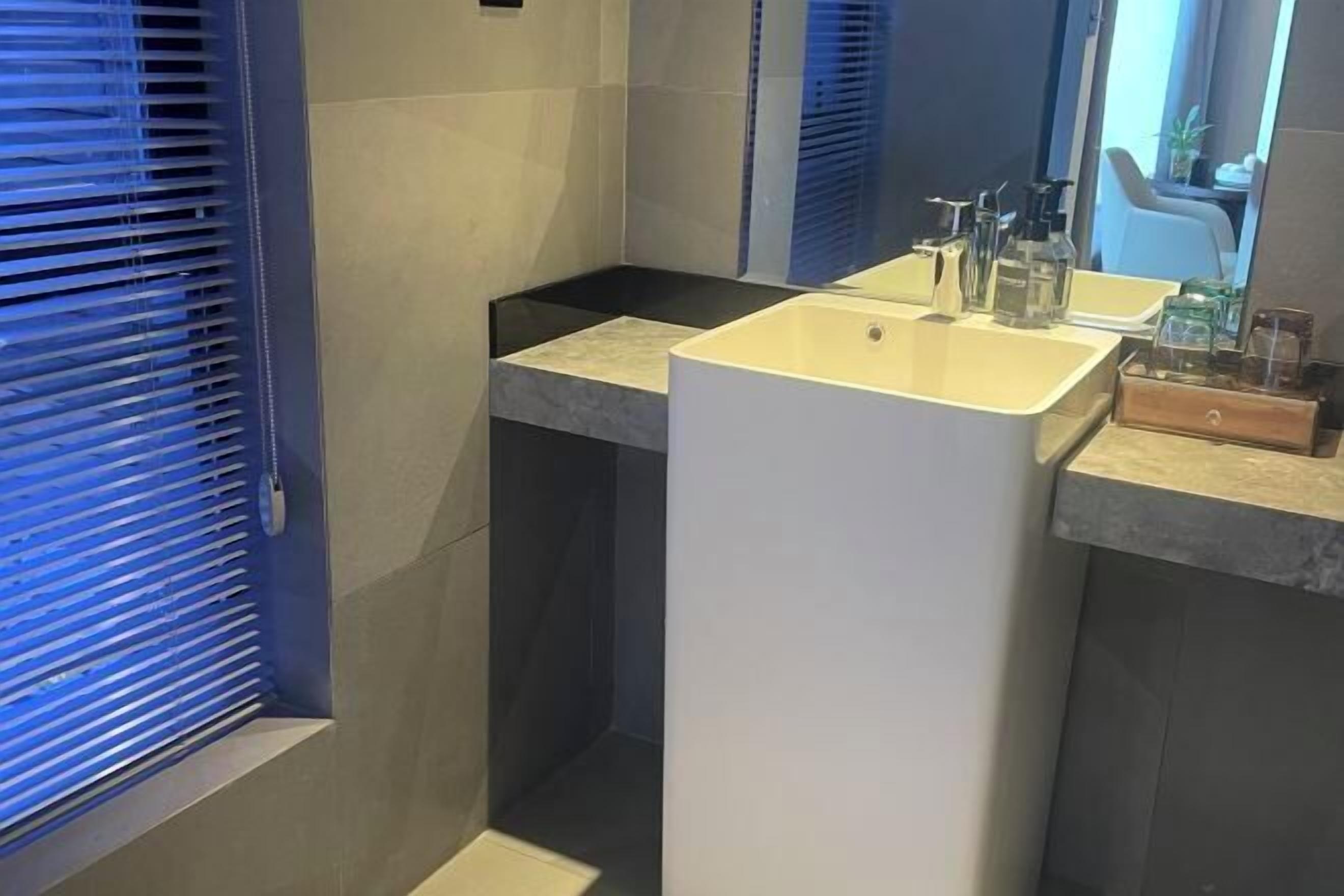 A modern bathroom with a large white sink, dark tiles, and a mirror.