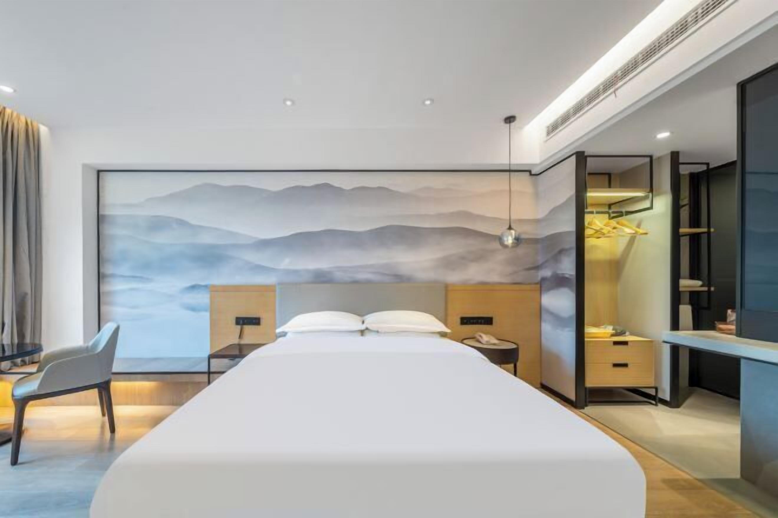 A modern hotel room with a large bed, a desk with a chair, a nightstand, and a wall-mounted TV.