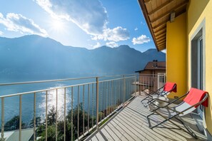A balcony with a view of a lake and mountains, featuring a yellow building and a red towel on a chair. - Ka Doro With Lake View (Nesso)