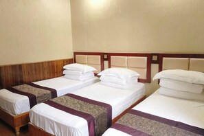 Habitación de hotel con cuatro camas individuales alineadas, cabeceras de madera y piso de madera.