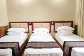 Habitación de hotel con tres camas individuales, cada una con cabecero de madera y ropa de cama blanca.
