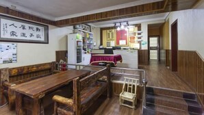 A dining area with a wooden table and benches, a refrigerator, and a kitchen in the background. - Guojia Courtyard Inn (Zhangjiajie)