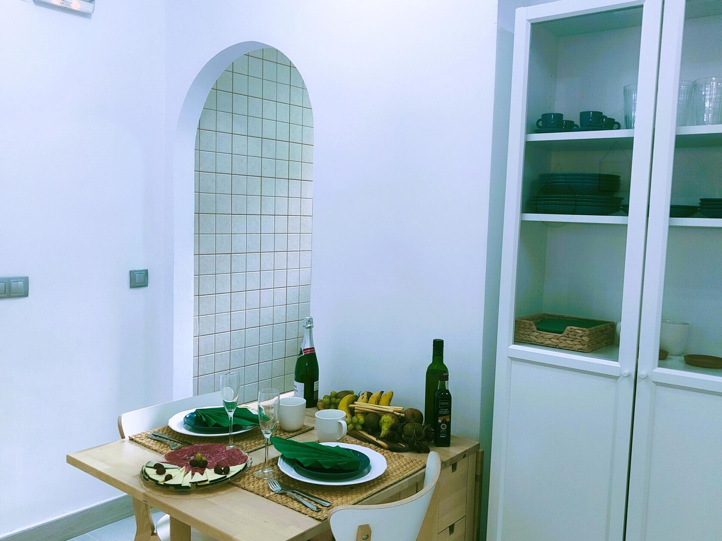 Et spisebord dækket med tallerkener, glas og bestik, samt en vinflaske og en kurv med frugt.
