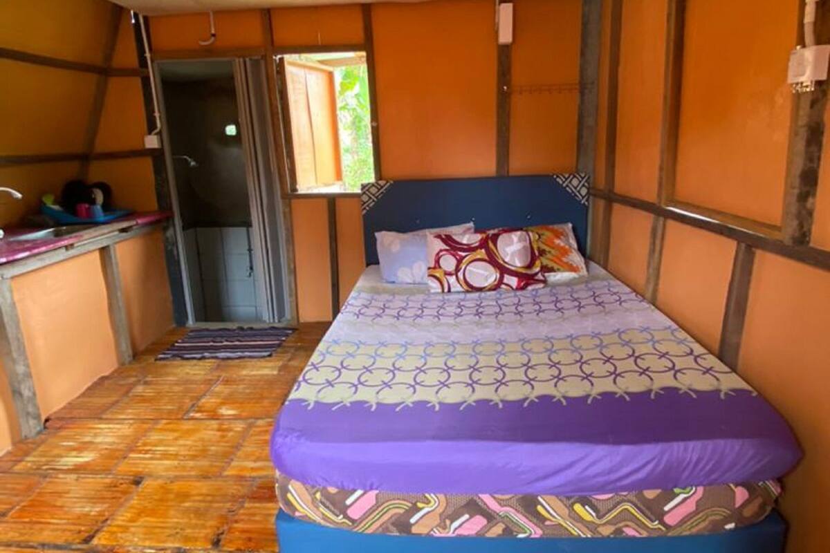 A single-bed room with a patterned bedspread, wooden flooring, and a window with a view.