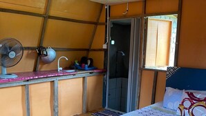 Una habitación con cama, un escritorio pequeño con ventilador, una ventana y zona de ducha.