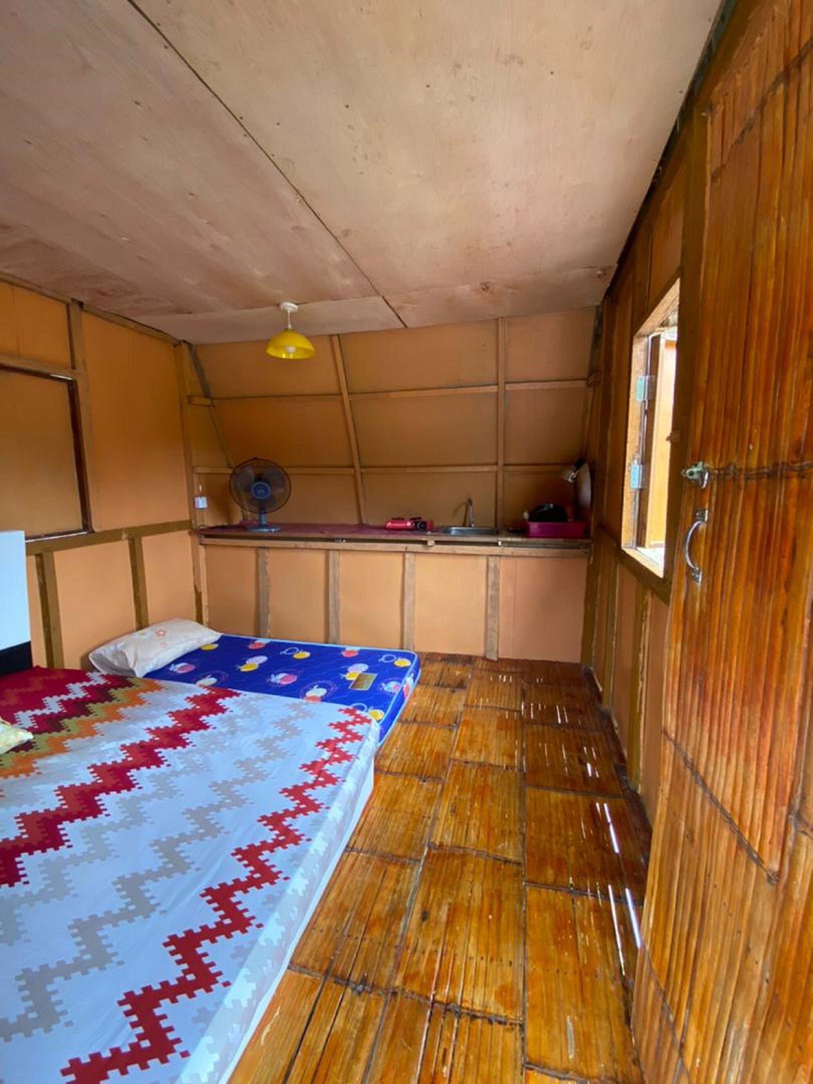 A compact room with a bed, a small desk, a fan, and a window.