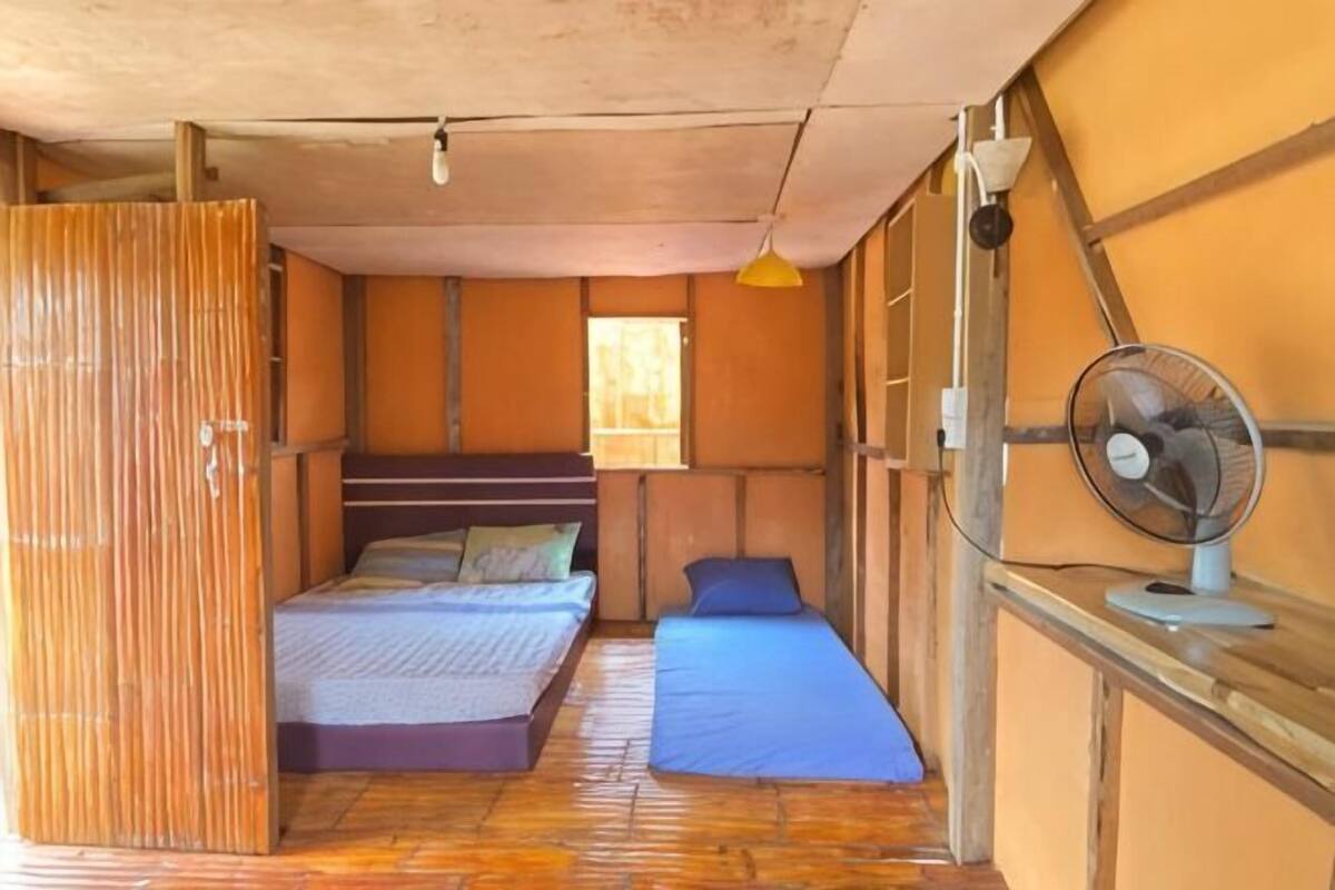 A room with a bed, a small table, a fan, and a window.