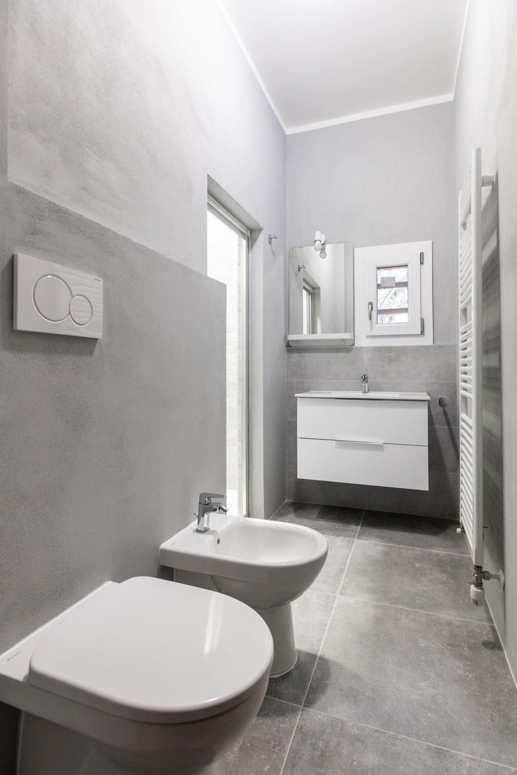 A modern bathroom with a toilet, bidet, and a sink with a mirror above.