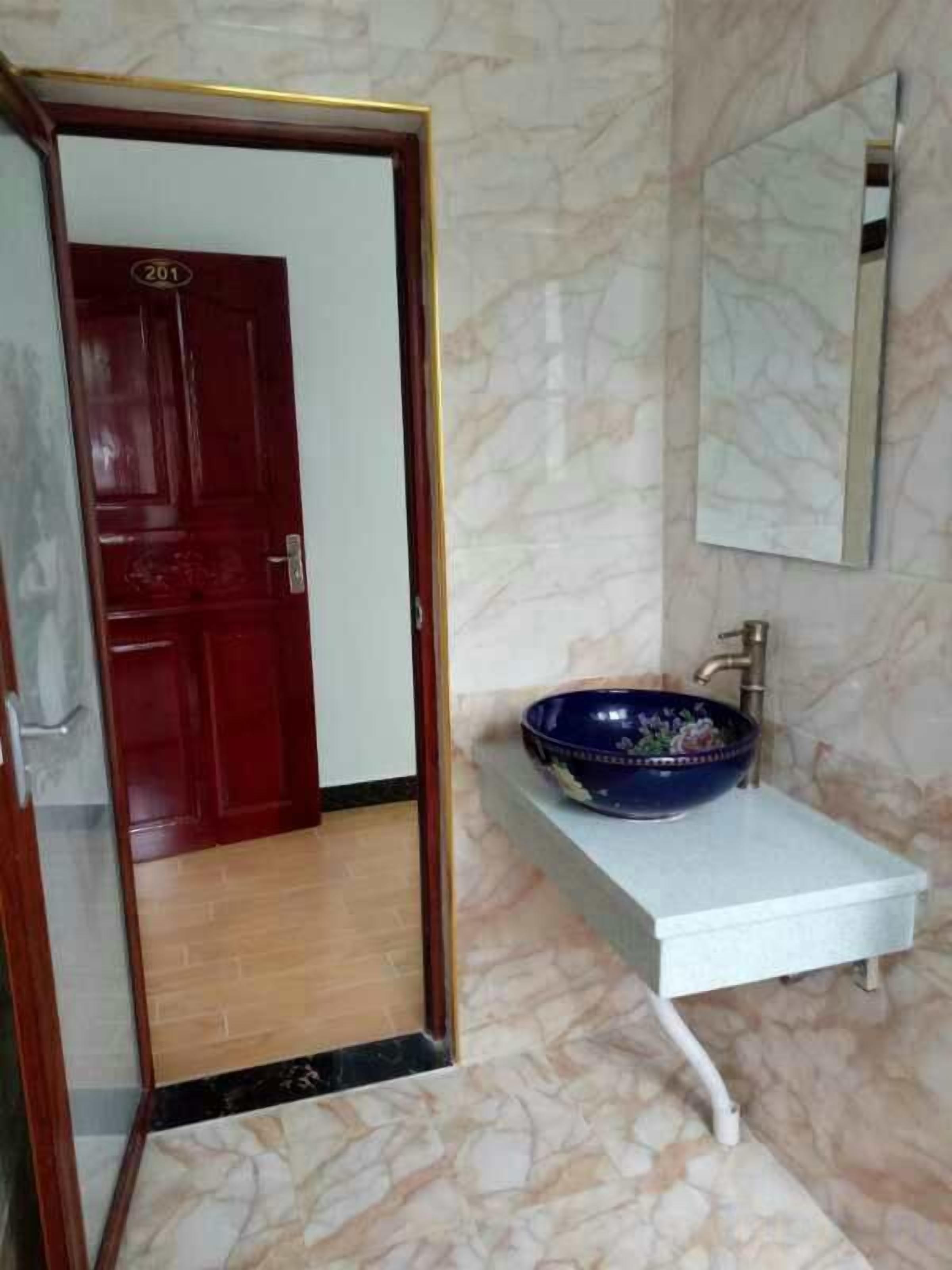 Une salle de bain avec un sol en marbre, un lavabo blanc, un bac bleu, une porte rouge et un miroir au mur.