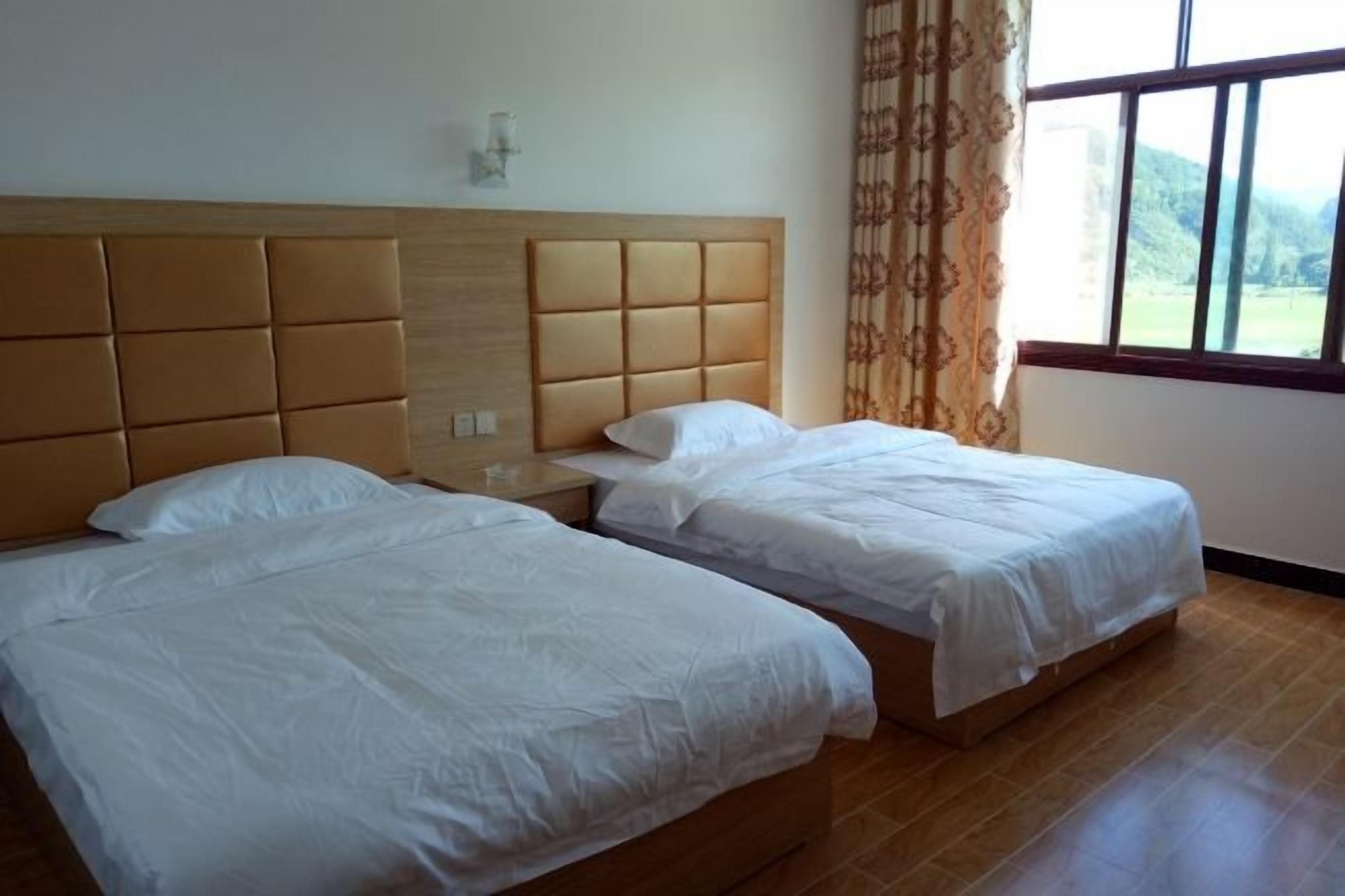 A room with two beds, a wooden headboard, a nightstand, and a window with curtains.