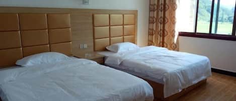 A room with two beds, a wooden headboard, a nightstand, and a window with curtains.