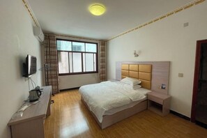 A hotel room with a bed, a desk with a kettle, a TV, and a window with curtains. - Langshan Patriotic Farm (Xinning)