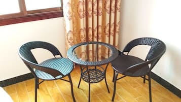 Une petite table ronde avec deux chaises, une fenêtre avec des rideaux et un sol carrelé.
