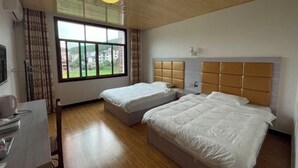 A hotel room with two beds, a desk, and a window with a view of buildings. - Langshan Patriotic Farm (Xinning)