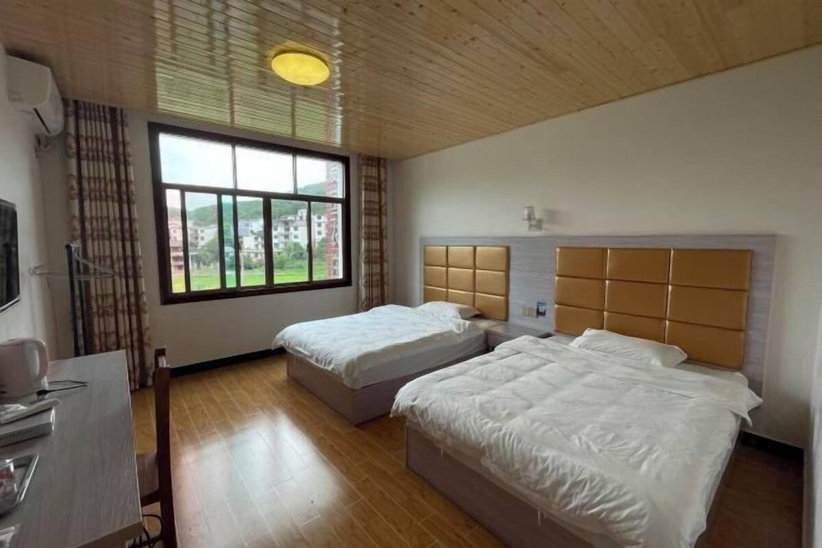 A hotel room with two beds, a desk, and a window with a view of buildings.