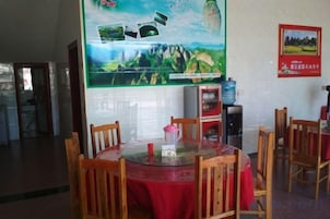 Un comedor con una mesa redonda cubierta con un mantel rojo, rodeada de sillas de madera. Se observa un cartel en la pared detrás de la mesa y un dispensador de agua a la derecha.