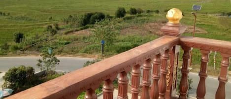 A balcony with a view of a green landscape and a road.