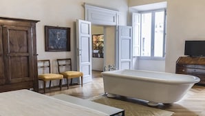 Un baño con bañera, muebles de madera, televisión y ventana con persianas.