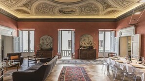 Una habitación amplia con techo alto, detalles ornamentales en el techo y un gran ventanal, con una zona de comedor dispuesta para una comida.