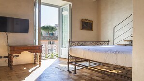 Un dormitorio con cama, televisión, escritorio y balcón.