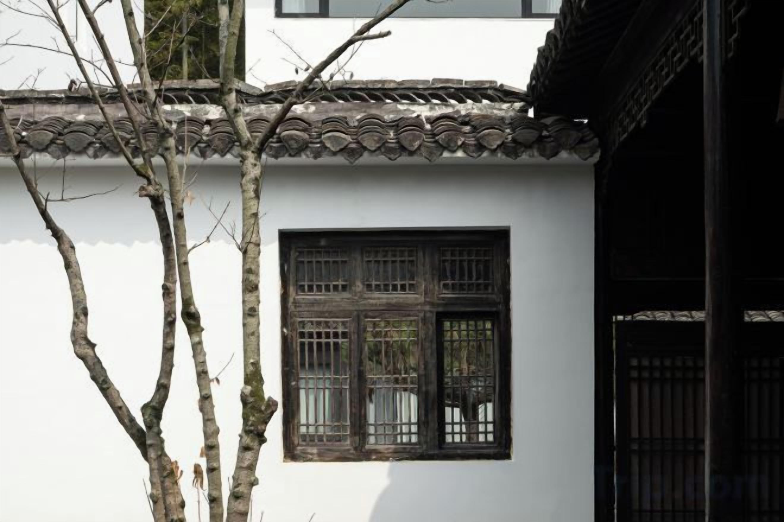 A traditional building with a tiled roof, a window with a grid pattern, and a tree in the foreground.