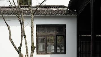 A traditional building with a tiled roof, a window with a grid pattern, and a tree in the foreground.