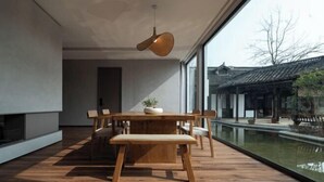 A modern dining area with a wooden table and chairs, a hanging light fixture, and a view of traditional architecture through large windows. - Huzhou Biocountry Resort (Changxing)