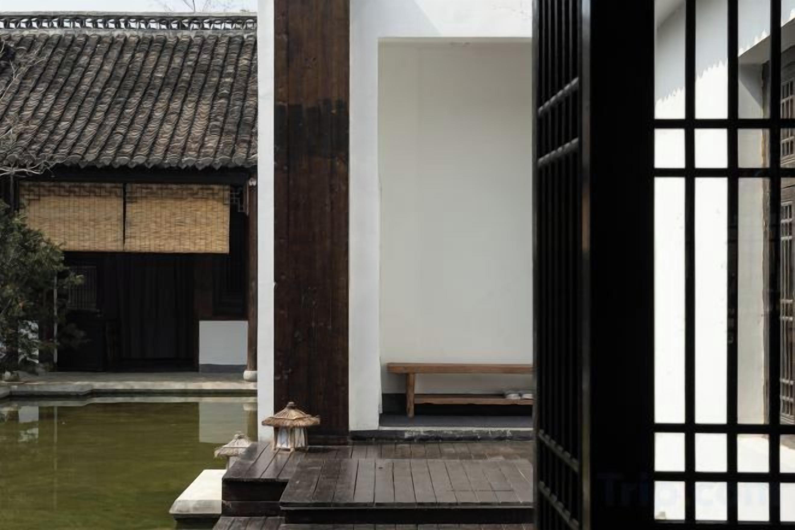 Un edificio japonés tradicional con una terraza de madera, un estanque pequeño y un banco de madera.