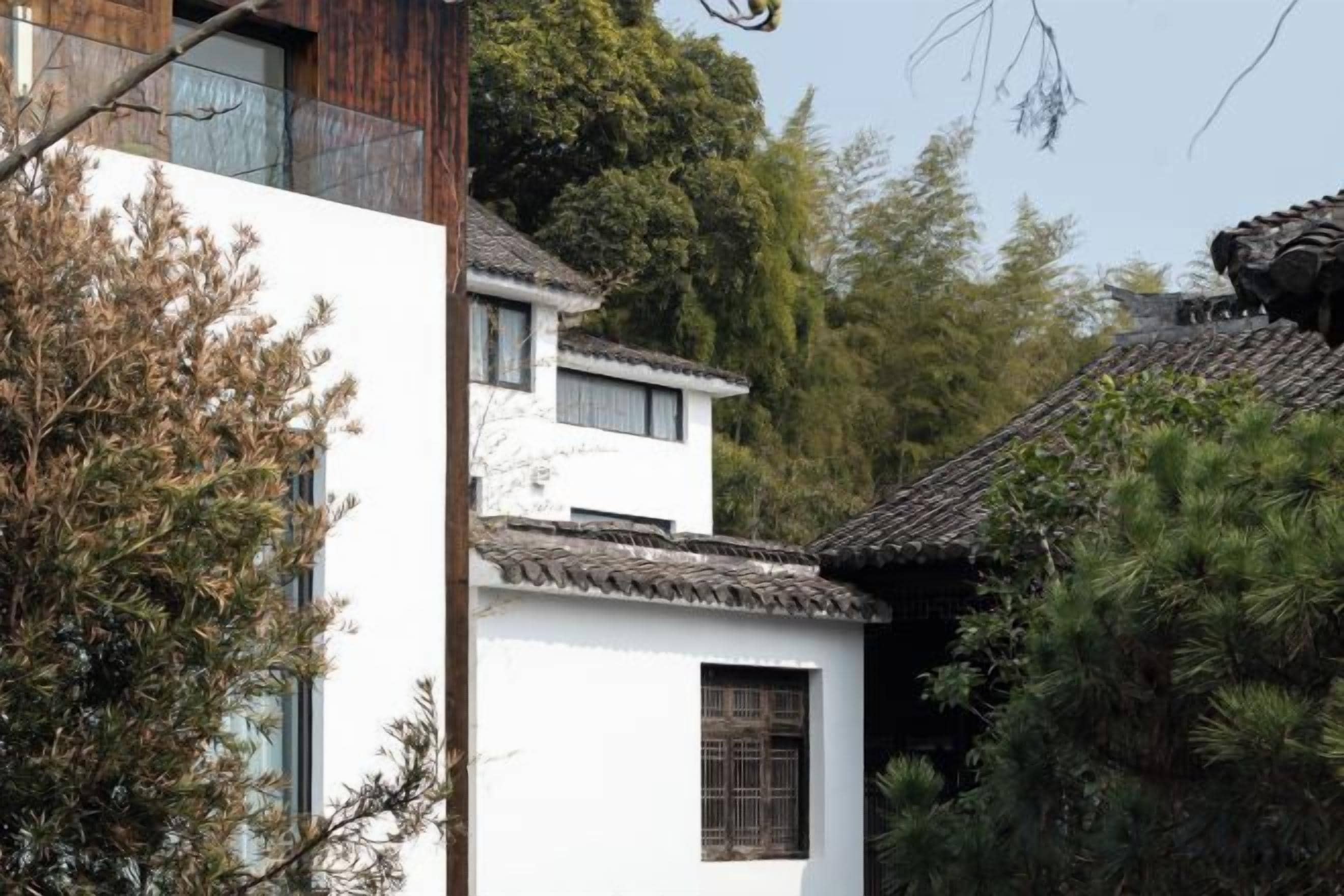 Un edificio tradicional con fachada blanca y tejado de tejas, rodeado de árboles.