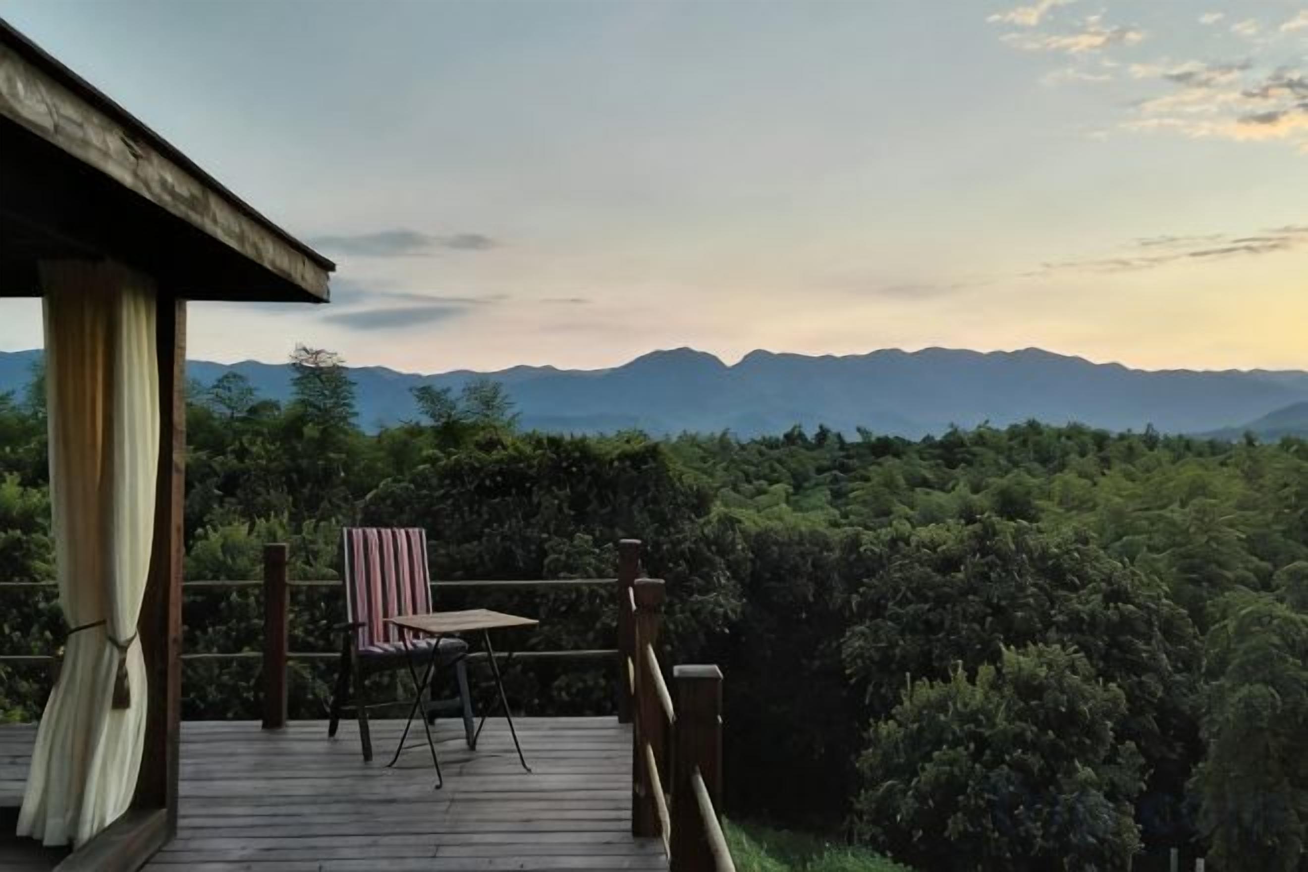 A wooden deck with a chair and table, overlooking a forested area and distant mountains.