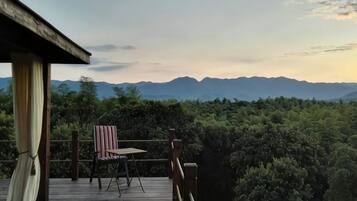A wooden deck with a chair and table, overlooking a forested area and distant mountains.