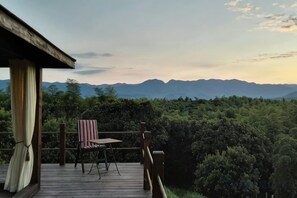 A wooden deck with a chair and table, overlooking a forested area and distant mountains.