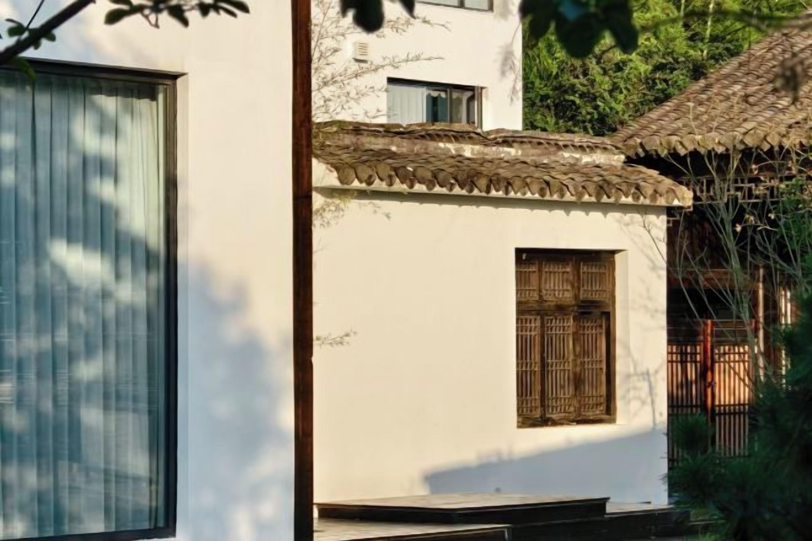 A traditional building with a tiled roof, a window with wooden shutters, and a small porch area.