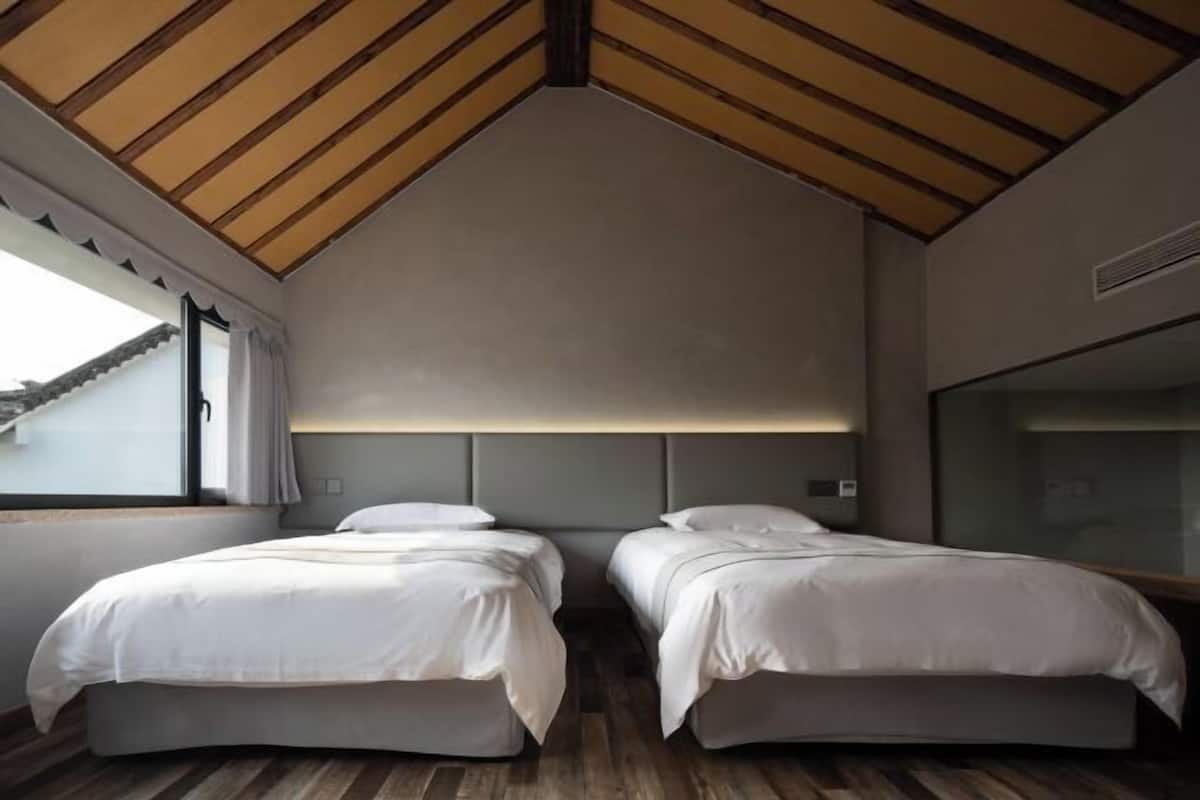 Une chambre avec deux lits, un plafond en pente et une fenêtre avec des rideaux.