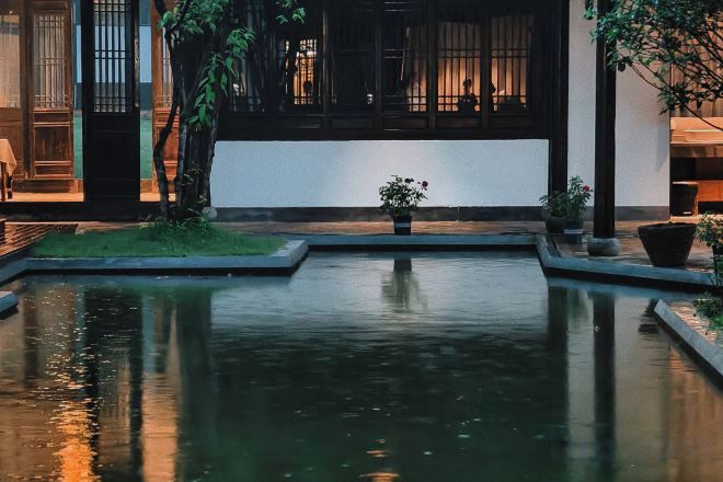 A tranquil courtyard with a reflective water feature, potted plants, and a traditional building facade.