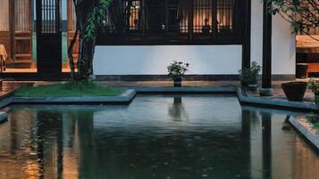 A tranquil courtyard with a reflective water feature, potted plants, and a traditional building facade.