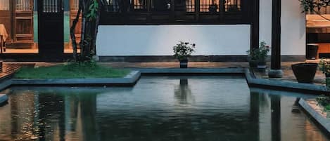 A tranquil courtyard with a reflective water feature, potted plants, and a traditional building facade.