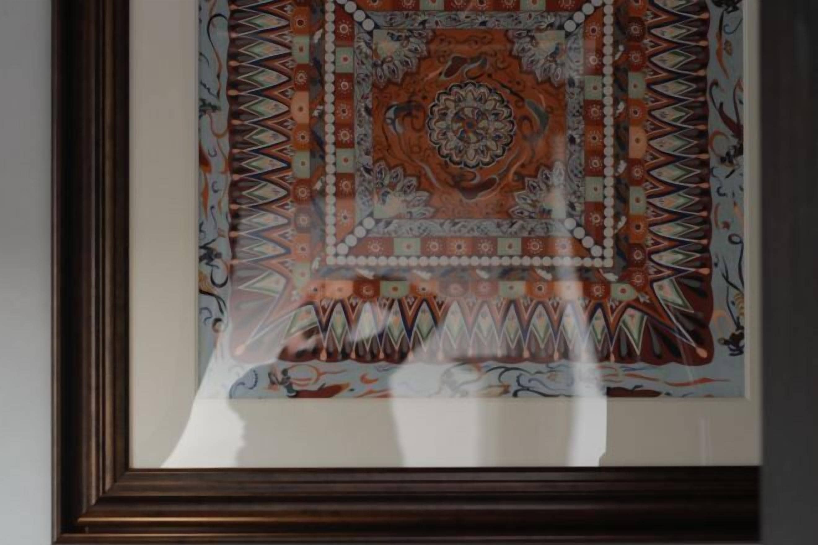 A framed artwork with a geometric and floral pattern, displayed on a wall.