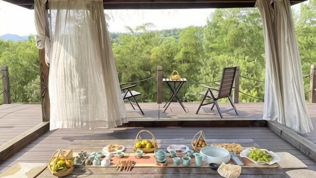 A covered outdoor area with a table set for a meal, surrounded by chairs and a scenic view. - Huzhou Biocountry Resort (Changxing)