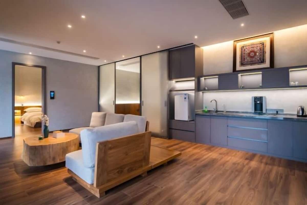 Une chambre d’hôtel moderne comprenant un lit, un petit coin salon, une kitchenette et un grand miroir.