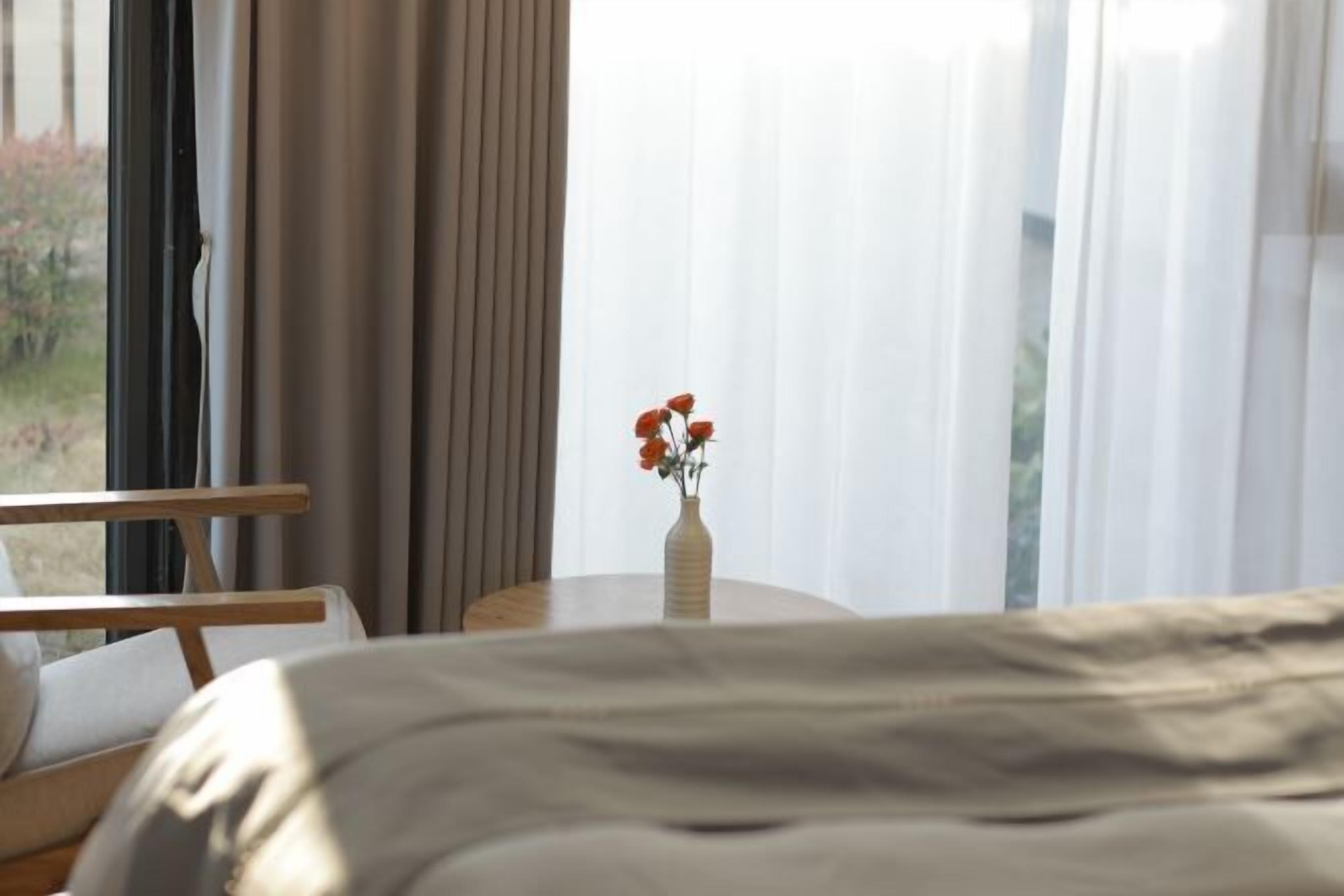 A hotel room with a bed, a wooden chair, a small round table, and a vase with flowers.