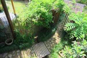 Un jardín con un sendero de piedra, un banco de madera y diversas plantas verdes.